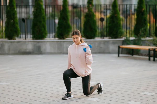 Chica de fitness joven haciendo ejercicios con pesas en el parque de la ciudad — Foto de Stock