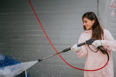 Araba yıkamada mavi araba yıkayan genç bir kadın.