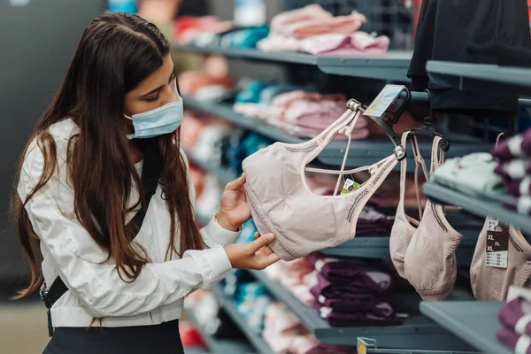 Chica comprador en la tienda con máscara médica, elegir underwea —  Fotos de Stock