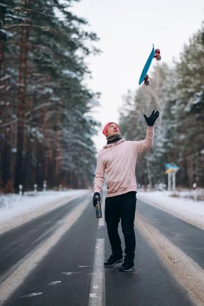 Skateboarder de pé na estrada no meio da floresta, cercado por neve — Fotografia de Stock