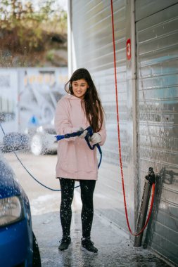 Yüksek basınçlı bir hortumdan esmer bir kadın arabaya temizlikçi yerleştirir.