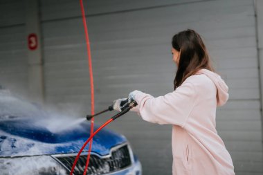 Araba yıkamada mavi araba yıkayan genç bir kadın.