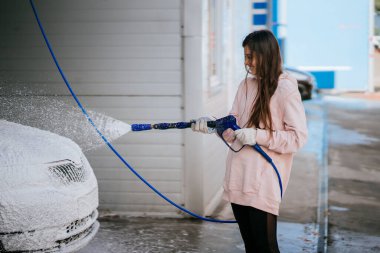 Yüksek basınçlı bir hortumdan esmer bir kadın arabaya temizlikçi yerleştirir.