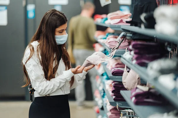 Chica comprador en la tienda con máscara médica, elegir underwea —  Fotos de Stock