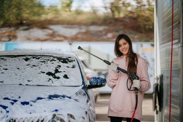 Yüksek basınçlı bir hortumdan esmer bir kadın arabaya temizlikçi yerleştirir. — Stok fotoğraf