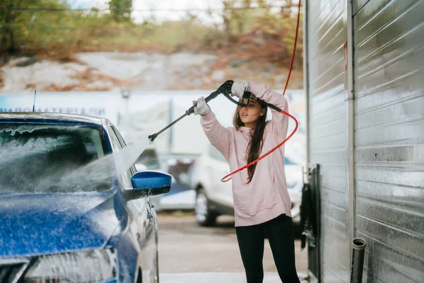 Mujer joven lavando coche azul en el lavado de coches — Foto de Stock
