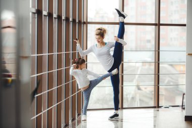 Anne kızına bacak esnetmeyi öğretiyor.