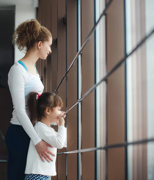 Kaksi eri-ikäistä tyttöä tuijottaa ikkunasta kuntosalilla. — kuvapankkivalokuva