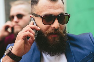 İki sakallı iş adamı telefona bakıyor.