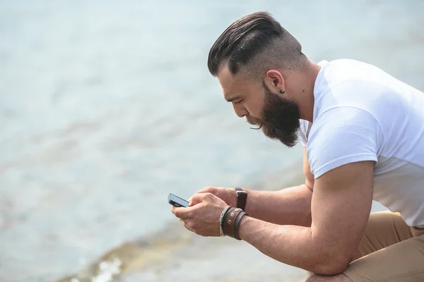 Homem barbudo americano usando telefone perto do rio — Fotografia de Stock