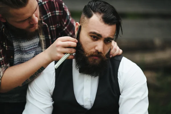 Barbero afeita a un hombre barbudo —  Fotos de Stock