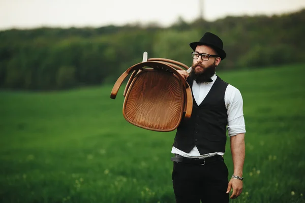 L'uomo barbuto porta una sedia sul campo — Foto Stock