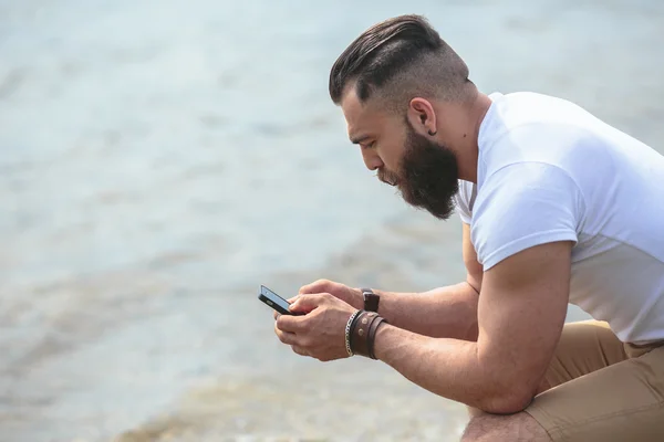 Homem barbudo americano usando telefone perto do rio — Fotografia de Stock