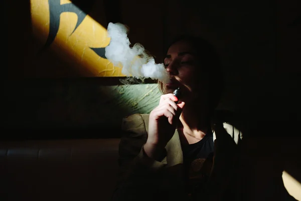 Tyttö istuu ja polttaa sähkösavuketta — kuvapankkivalokuva