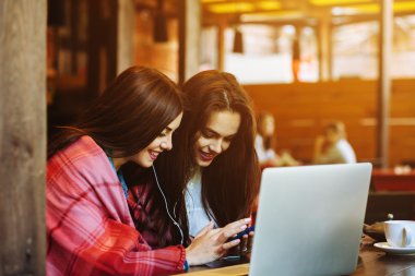 İki kız oturmuş akıllı telefonuyla müzik dinliyor.