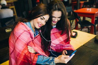 İki kız oturmuş akıllı telefonuyla müzik dinliyor.