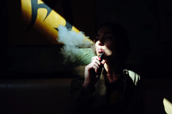 Girl sits and smokes electronic cigarette — Stock Photo, Image