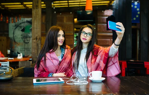 İki yakın arkadaş kafede selfie çekiyorlar.