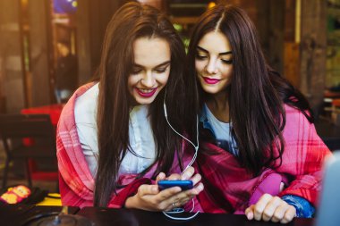 İki kız oturmuş akıllı telefonuyla müzik dinliyor.