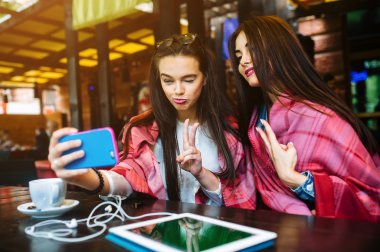 İki yakın arkadaş kafede selfie çekiyorlar.