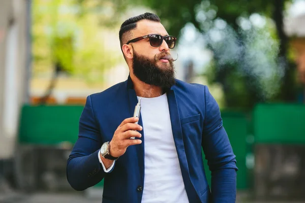 Человек с бородой курит электронную сигарету — стоковое фото