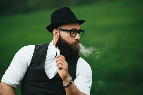 Man med ett skägg röker elektronisk cigarett — Stockfoto