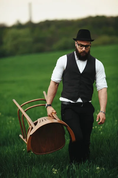 Bärtiger Mann trägt einen Stuhl auf dem Feld — Stockfoto