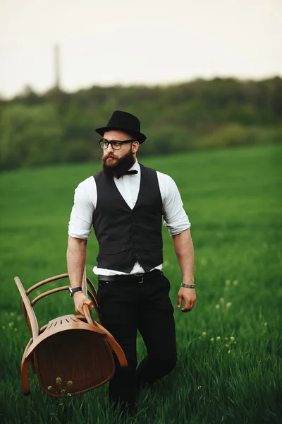 Бородатий чоловік несе стілець на полі — стокове фото