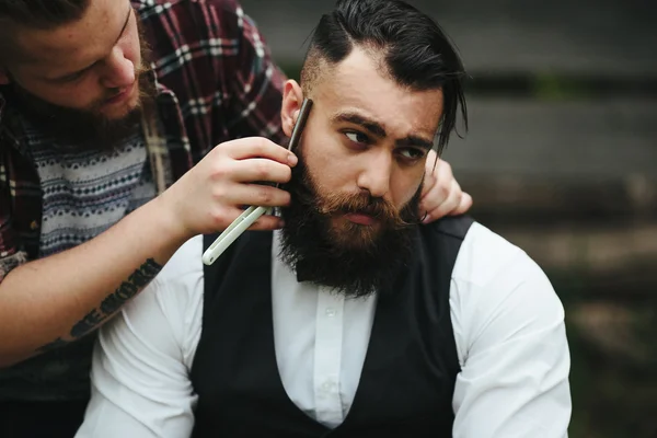 Barber shaves a bearded man — Stock Photo, Image