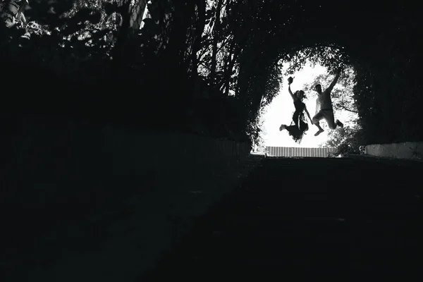 Casal pulando no final do túnel com árvores — Fotografia de Stock