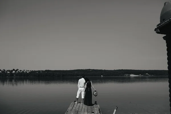 Jovem casal de pé em um convés junto à água — Fotografia de Stock