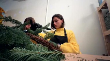 Bitmiş beyaz çelenk satıcısı el yapımı ürün yüzüğünü sunuyor, butik masasında süs, kurdele ve yeşillik yakın plan