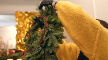 Çam çelengi mumlarını düzenleyen yakın çekim elleri, sıcak stüdyo ışığı, görünür sarı süveter, dairesel biçimli yeşil dallar.,