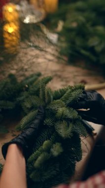 Kadın tatil yeşilliklerini süslüyor, kadın mum ışığı ve parlak ışıklarla aydınlatılmış ladin dallarını dikkatlice hazırlıyor.