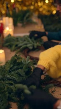 Tezgahtaki köknar dallarını mumlarla ve bokeh arkaplanıyla düzenleyen eller, el işçiliği titreşimleri, çiçekçilik süslemeleri.