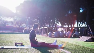Siyah kadın parkta oturmuş, serinliyor, dizleri açık nefes alıyor, arka lambası yumuşak, jimnastik takımları düzgün yerleştirilmiş.