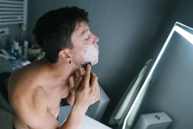 Ayna köpüklü üstsüz adam, köpüklü dikkatli tıraş öncesi köpük köpüğü köpüklü sabun köpüğü, tuvalet malzemesi ve odaklanmış ifade, samimi.