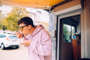 Adam sıcak çorbayı kaldırım kafesinde içiyor, sıcak kase ve kaşık sıcacık duruş, pembe kapüşonlu ve gözlüklü.,