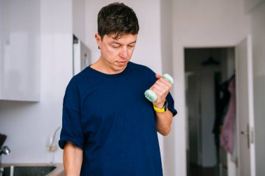 Mutfakta ilaç kutusu etiketi okuyan, endişeli bir ifade, donanma gömleği ve kol saati, tezgah ve dolapların yanında duran bir adam.,