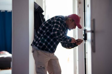 Kiracı sorun çıkarma dairesinin kapısına sıkışmış, diz çöküp tornavida ve tork ile nazikçe baskı uyguluyor.