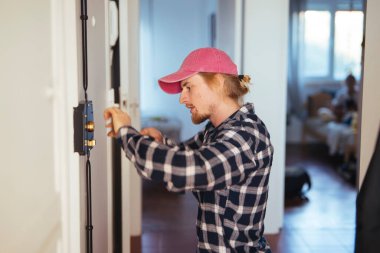Kilit değiştirme işlemini apartman girişinde tamamlayan çilingir, kilit hizalaması doğrulanıyor ve döndürme işlemi test ediliyor, odaklanmış eller