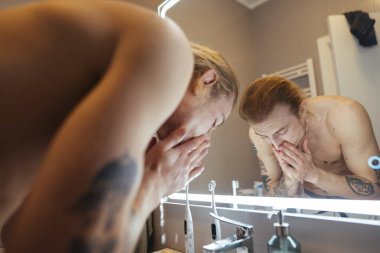 Beyaz adam ayna ışığı altında durulanıyor, sakin bir akşam, kolları dövmeli, banyo sıcaklığı, her gece.