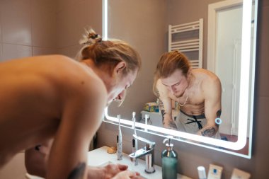 Tişörtsüz adam aynada yansıma, derin düşüncelere dalma, sabit duruş, düşünceli bir şekilde güne hazırlanma.