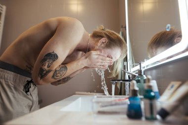 Aydınlatılmış aynaya su sıçratan üstsüz adam, dinamik hareket, ışığı yakalayan damlacıklar, erken dönem gizli enerjisi