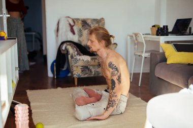 Dövmeli bir adam halının üstünde köpekle bağ kuruyor, rahat bir apartman ışığı. Sıcak bir sabah sahnesinde narin bir aşk, örülmüş bir süveter