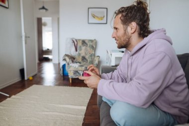 Kontrolörle video oyunu oynayan adam, yoğun odaklanma, günlük kapüşonlu, oturma odası zeminli, ekran hareketli, rekabetçi