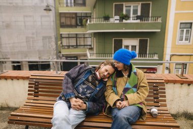 Ahşap bankta oturan çift, kafası omuzlarında ve huzurlu ifadeleri olan, rahatlamış şehir yürüyüşü sonrası, sıcak