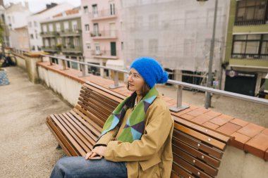 Sakin bankta oturan, yan bakan bereli ve katmanlı ceket, sakin pastel arka plan ve yaya geçidi.,