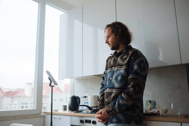 Mutfaktaki adam telefonu kontrol ediyor. Sabahları süveter ve telefon tomarı, yemek blogcusu enerjisi ve yemek tarifi planlama.