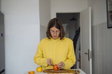 Tezgahta portakal dilimleyen genç bir kadın. Kesiklere ve yumuşak doğal ışığa odaklanmış. Sarı süveter ve gözlük takıyor.